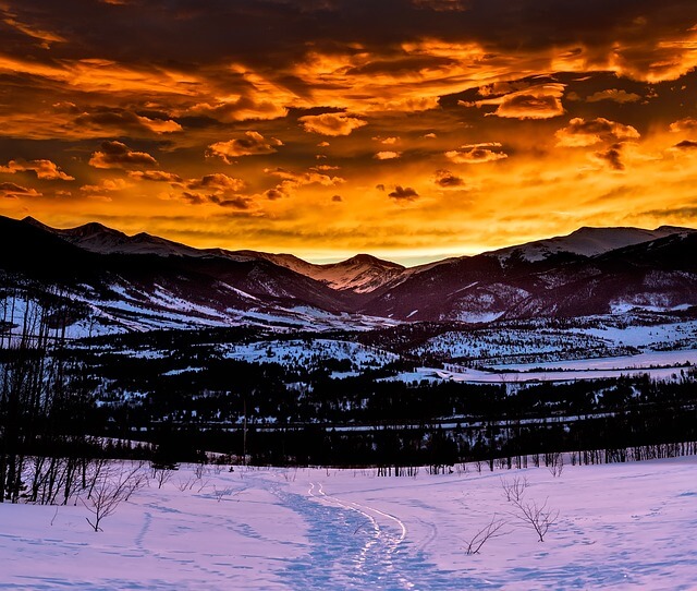 A scenic picture of a snowed in meadow with mountains in the background during sunset hour