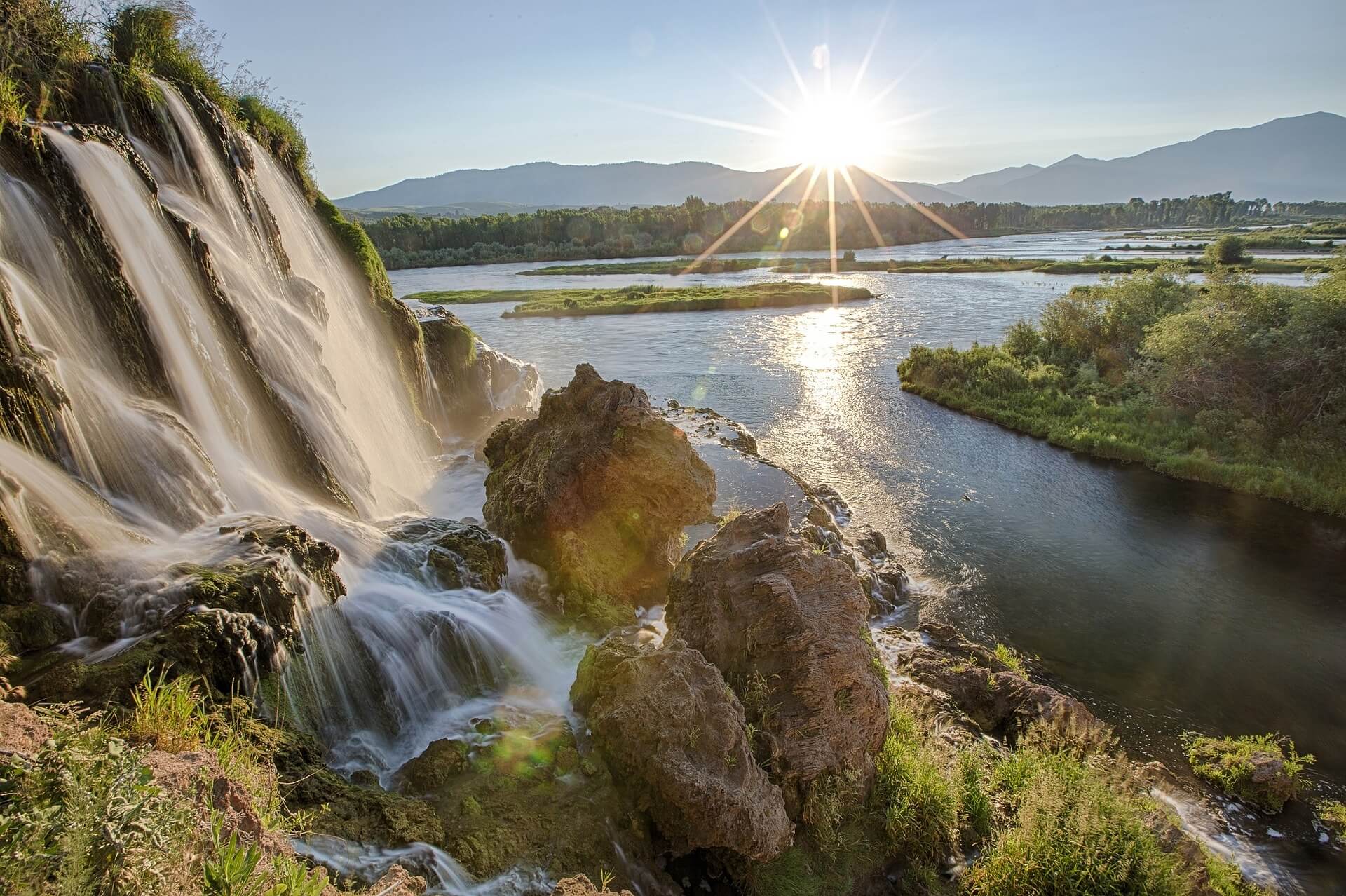 A picture of a waterfall running into the Snake River with mountains in the background