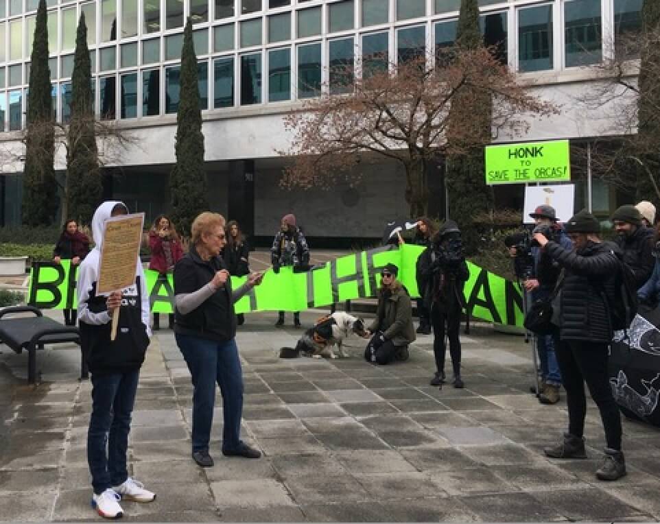 “March for Dam Breach” Kickoff Rally - March 1, 2020, Corps of Engineers and Bonneville Power Administration Complex, Portland  |  Cole Sitter holding Cease & Desist poster for Krestine Reed, reading to the crowd.